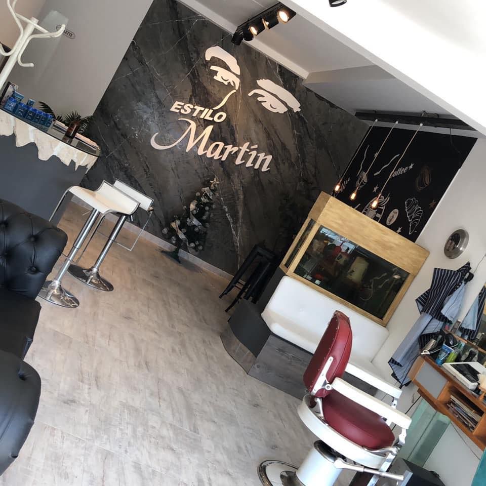 Vista interior de una barbería moderna llamada Estilo Martin, que cuenta con una pared decorativa oscura