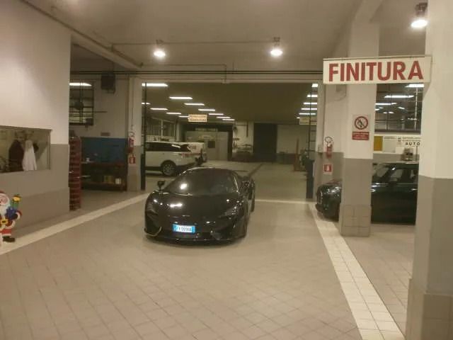 Un'auto sportiva nera in un garage, in avvicinamento all'uscita. Il cartello dice "FINITURA".
