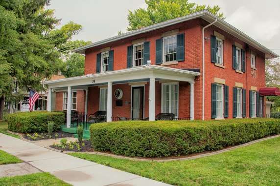 Two-story red brick house with white columns, green shutters, and a manicured lawn on a corner lot