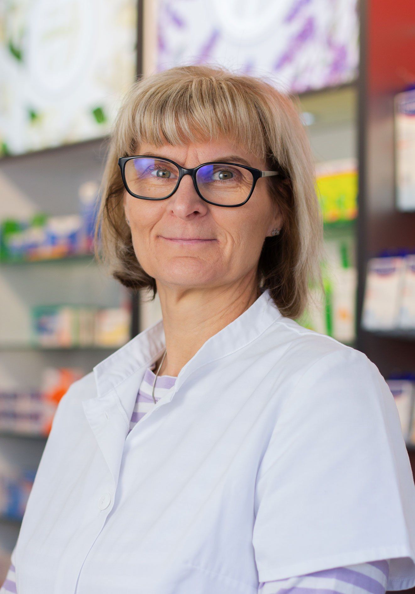 Eine Frau mit Brille und weißem Kittel steht in einer Apotheke.
