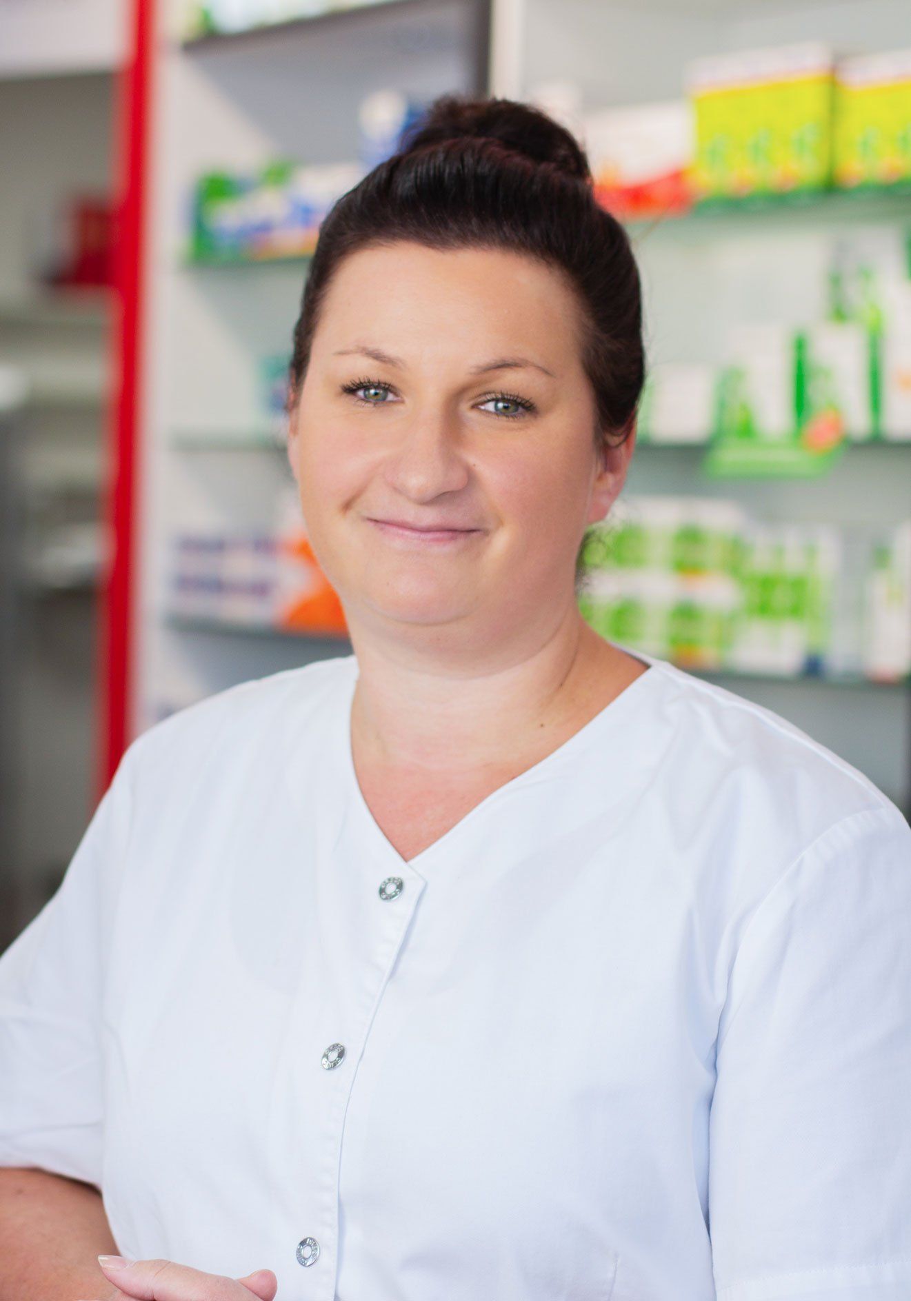Eine Frau in weißer Uniform steht vor einem Regal in einer Apotheke.
