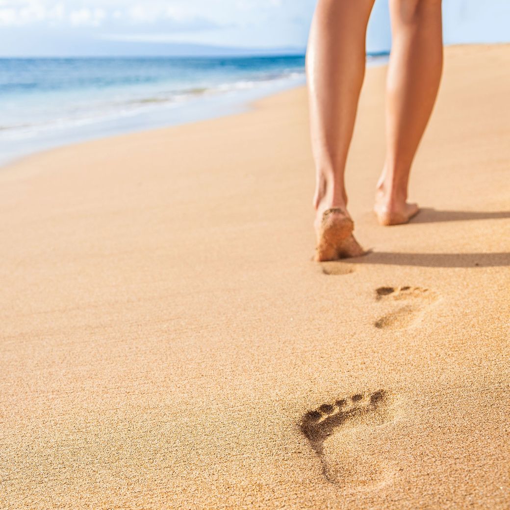 Eine Frau geht am Strand entlang und hinterlässt Fußabdrücke im Sand.