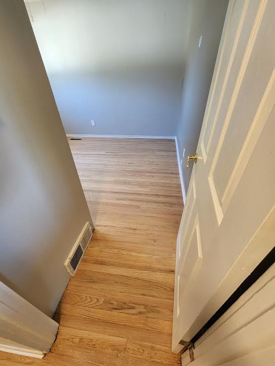 View down a hallway with wooden floors, grey walls, and a partially open white door.