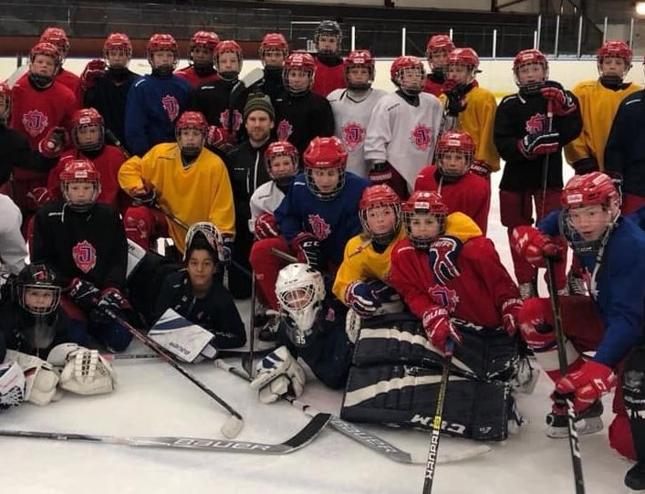 Stor grupp hockeyspelare i röda och gula tröjor poserar på isen med klubbor och utrustning