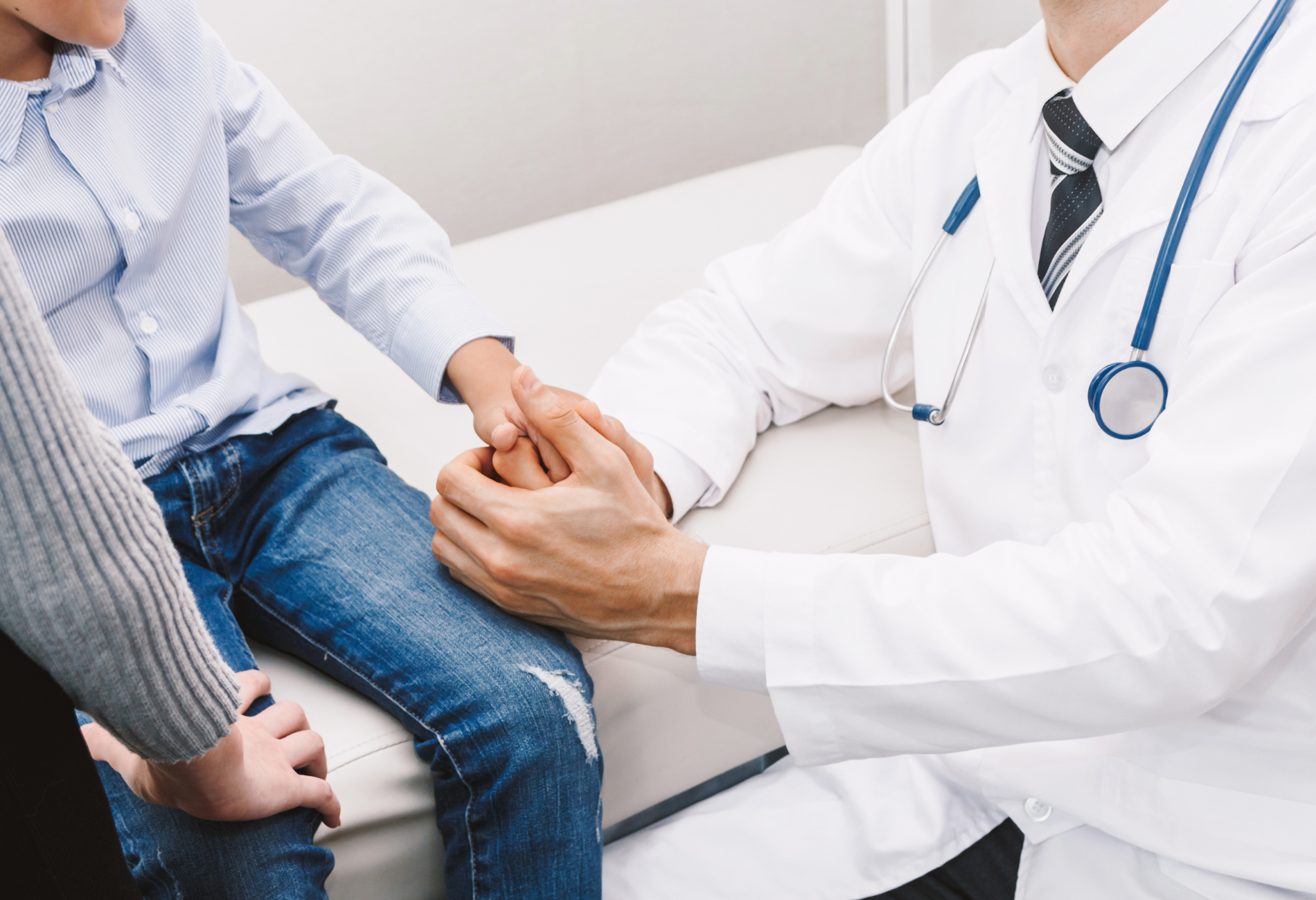 a doctor is holding the hand of a child who is sitting on a bed .