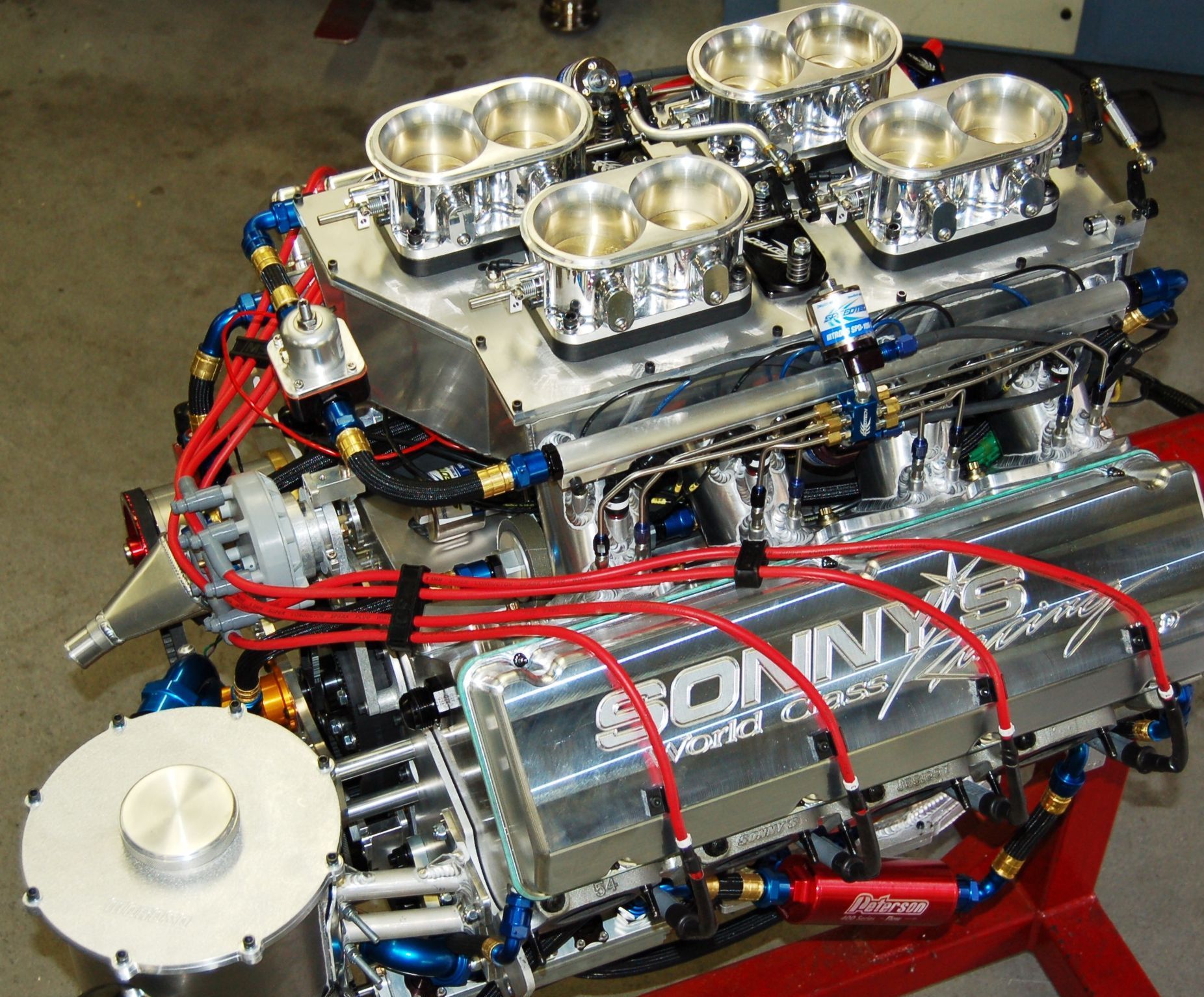 Polished V8 engine with chrome intake stacks and red tubing on a display stand