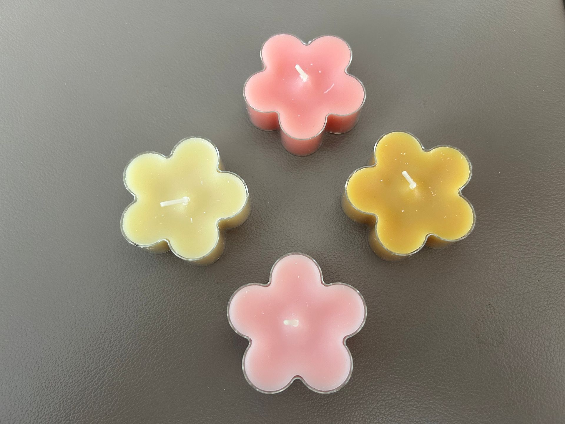 Vier pastelkleurige, bloemvormige waximelichtjes: roze, geel en oranje.