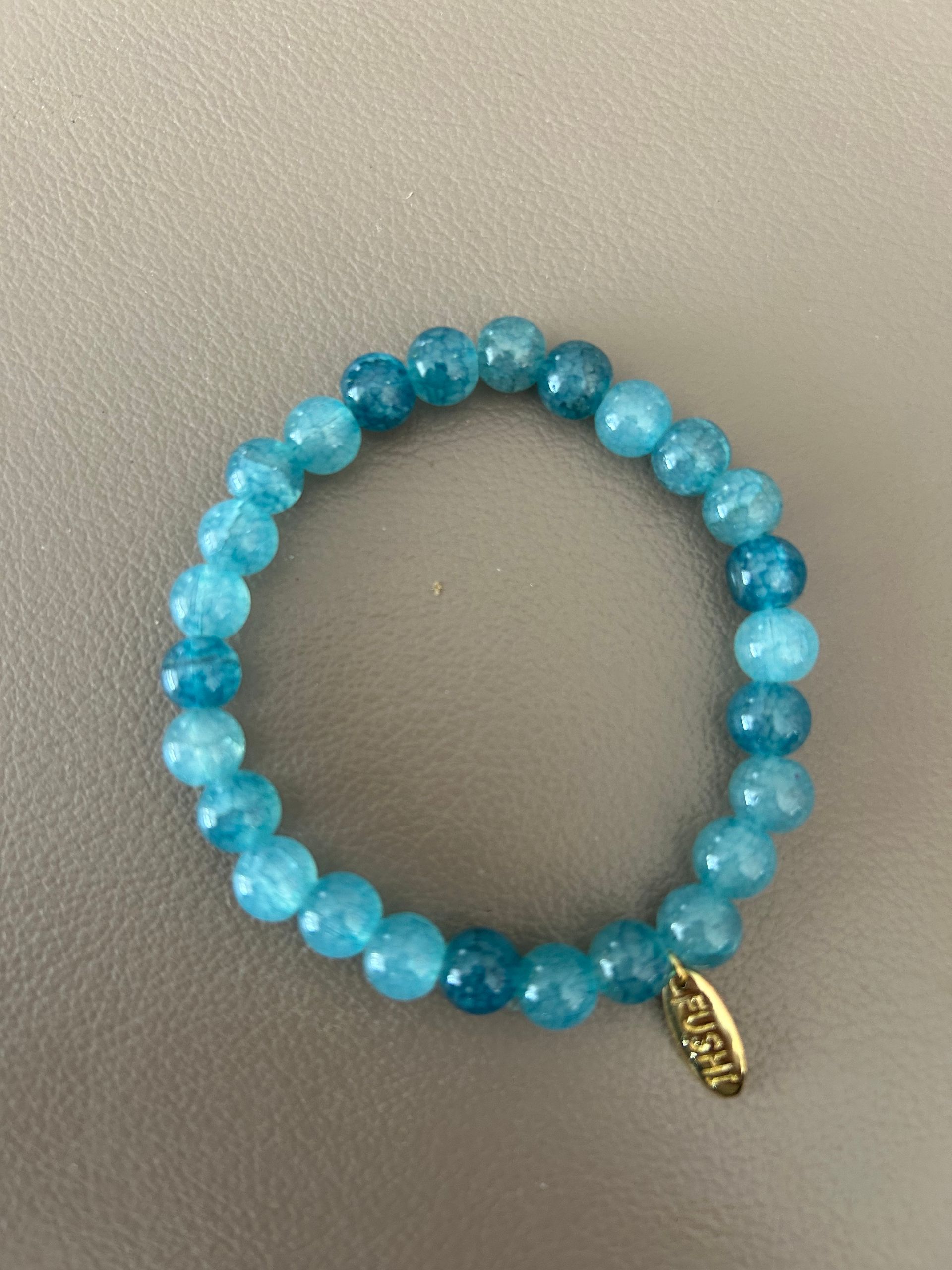 Glas kralenarmband turquoise /blauw met goudkleurig bedeltje van het merk.