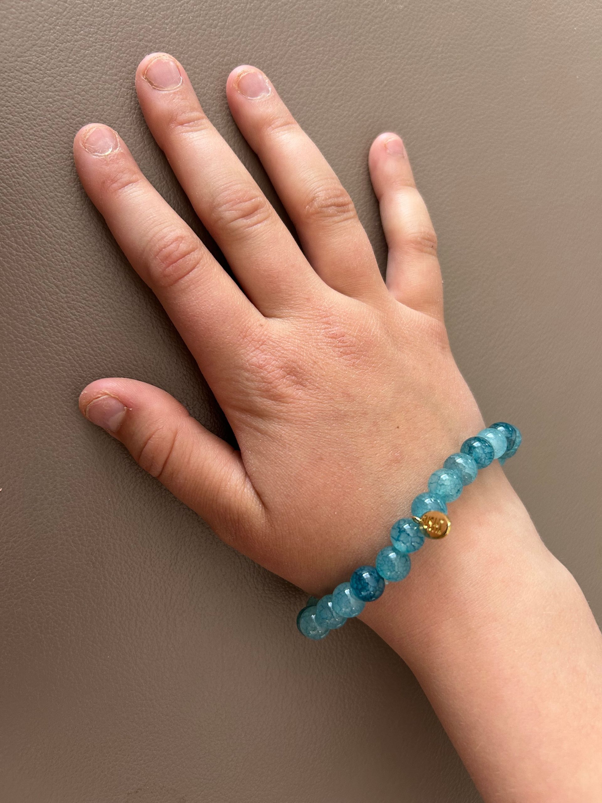Glas kralenarmband turquoise /blauw met goudkleurig bedeltje van het merk.