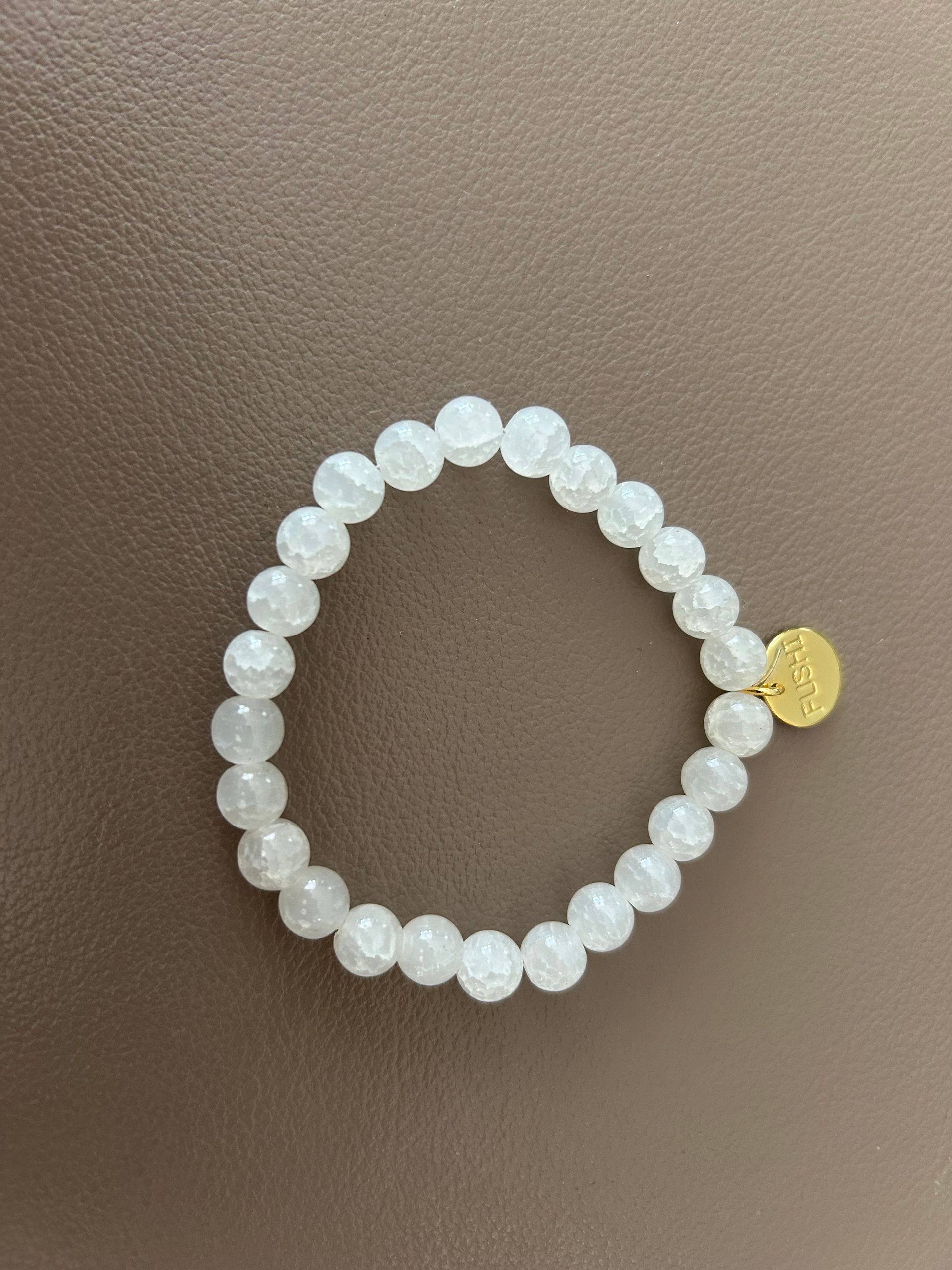 Witte glaskralenarmband met een klein gouden bedeltje.