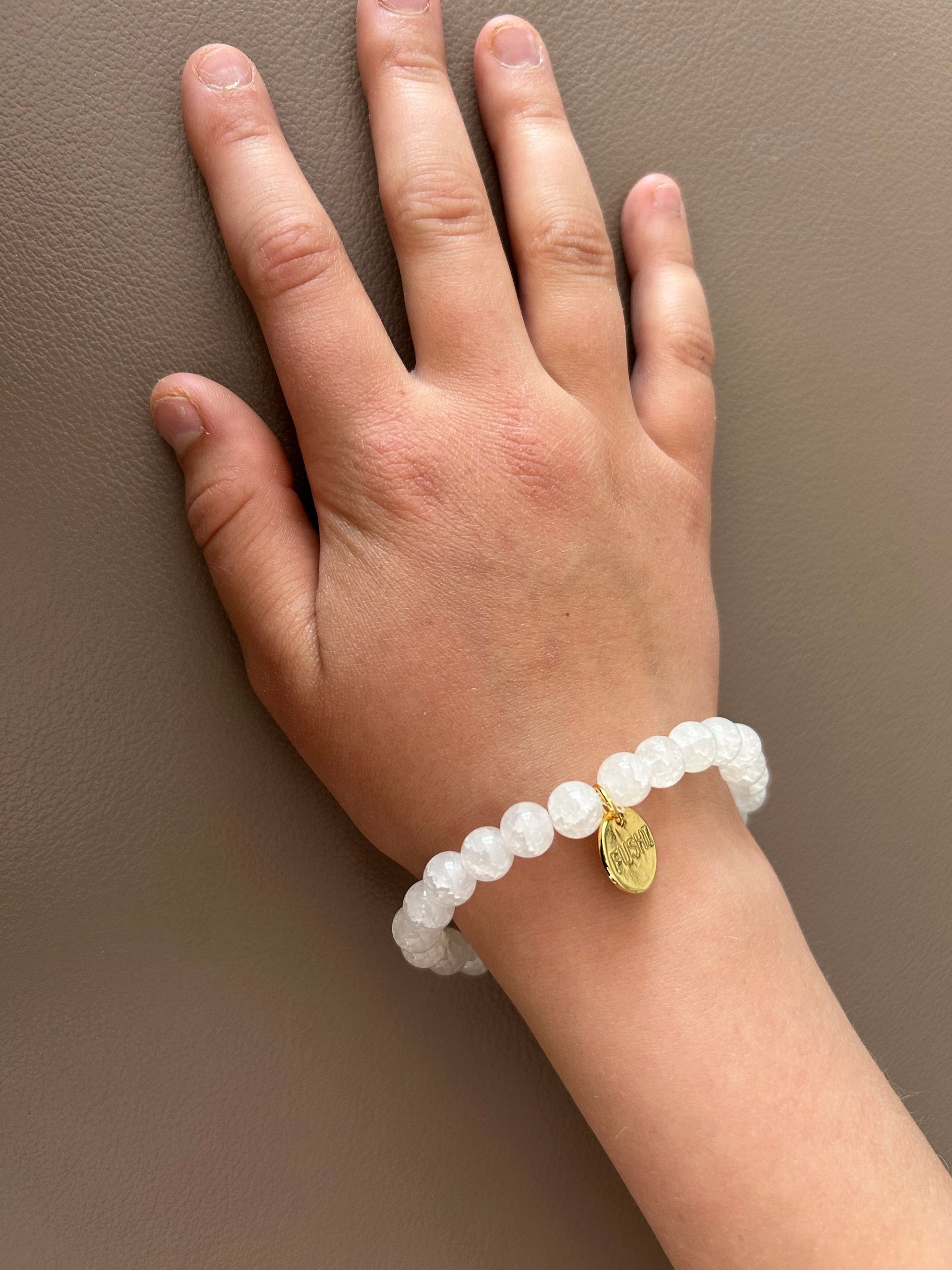 Witte glaskralenarmband met een klein gouden bedeltje.