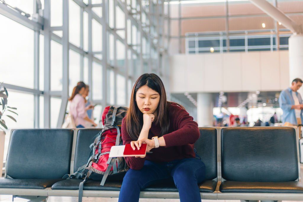 An Asian woman is sitting beside her backpack and looking at her watch.