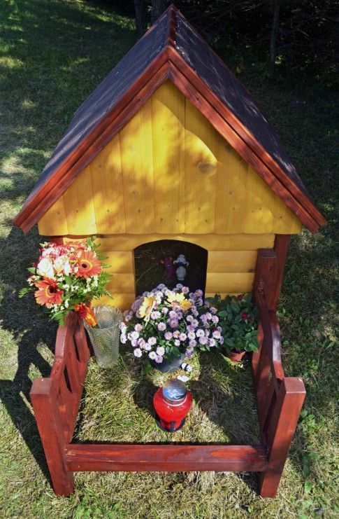 A Small Wooden Dog House With Flowers and a Candle in Front of It — Mini Digger and Trailer Hire in Mareeba, QLD