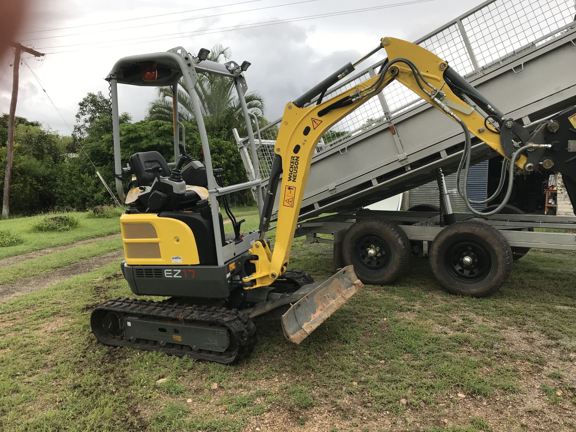 Yellow mini excavator next to a trailer on a grassy area.— Mini Digger and Trailer Hire in Atherton, QLD