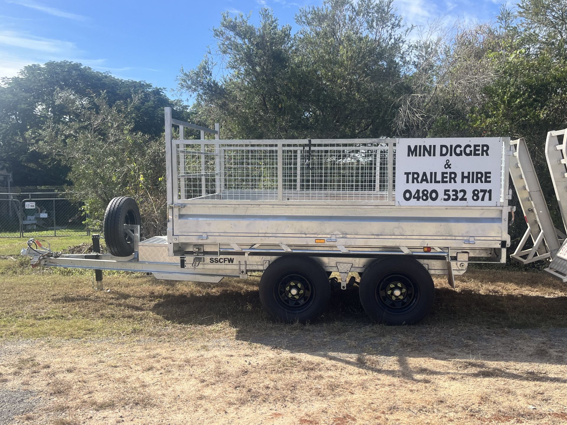 White trailer with cage, tire attached, parked outside with advertisement for