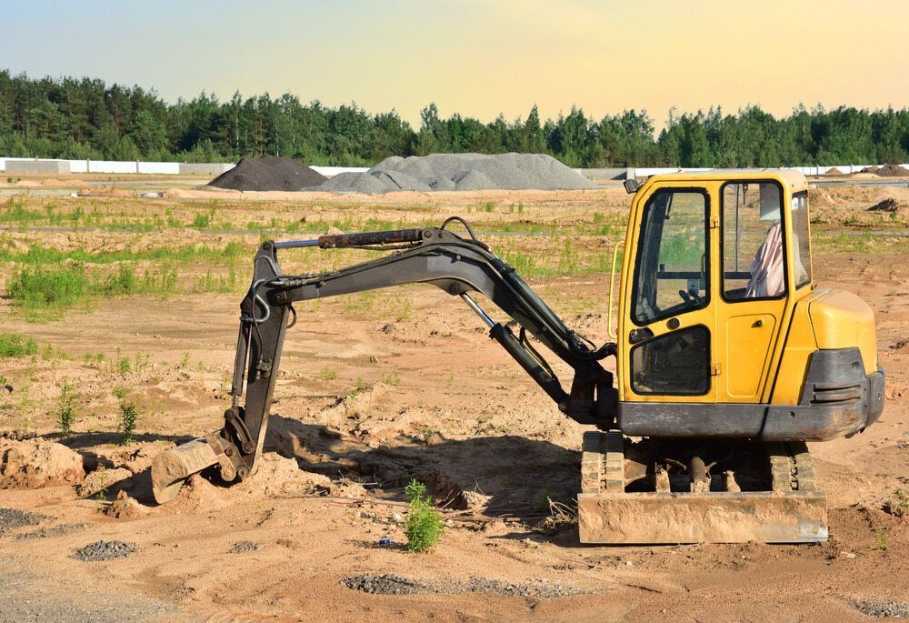 Yellow excavator on a construction site, arm extended, dirt and gravel piles visible in the background.— Mini Digger and Trailer Hire in Mareeba, QLD