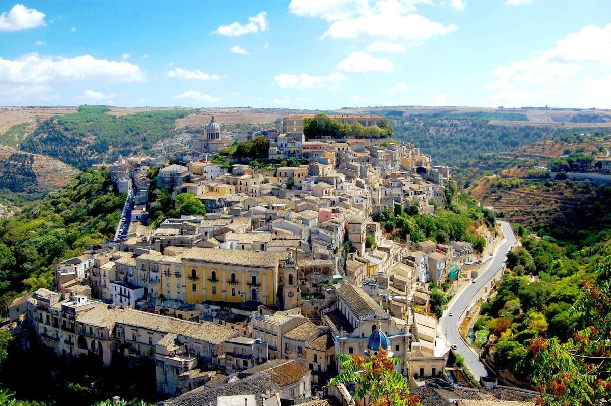 A hillside town with stone buildings and winding roads in a rocky valley under a bright sky