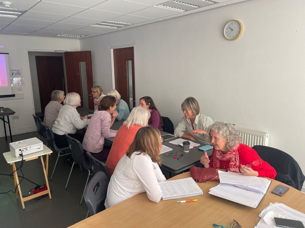 People seated around tables in a meeting room, discussing papers and laptops.
