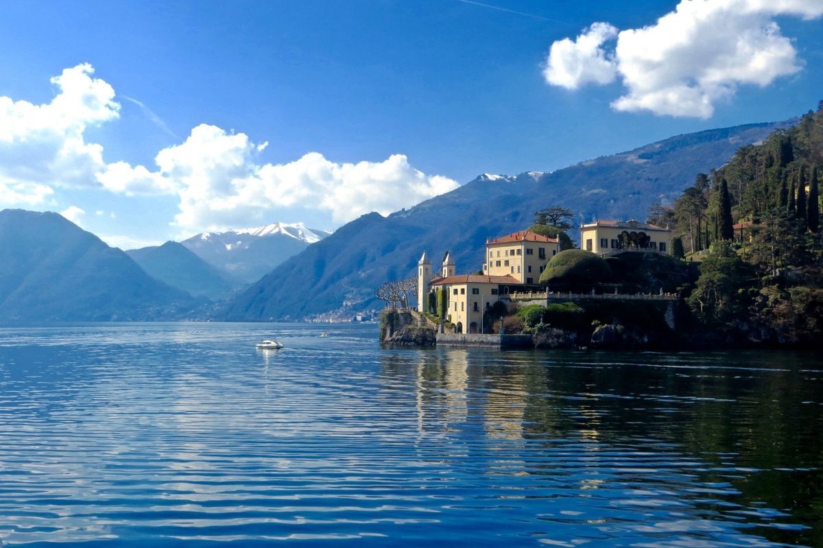 Lakefront village with colorful houses, calm blue water, and mountains under a bright sky