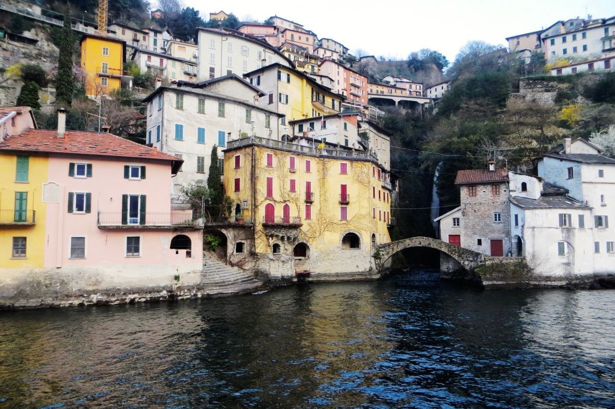 Colorful riverside houses and a stone bridge lining a calm waterfront town.