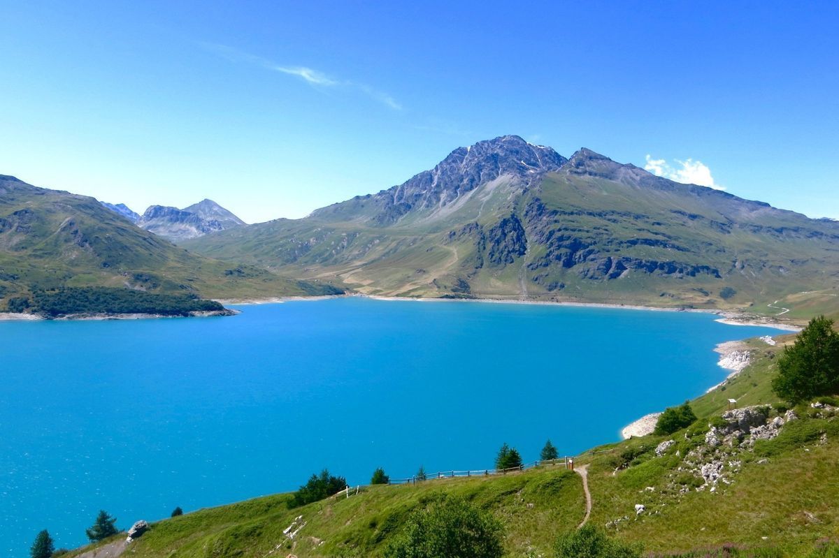 Blue mountain lake with a grassy shoreline and rocky peaks under a clear sky