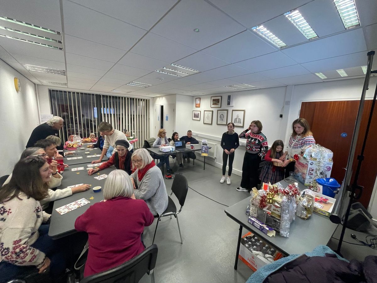 People gathered in a meeting room, socializing around tables with gift baskets and snacks.