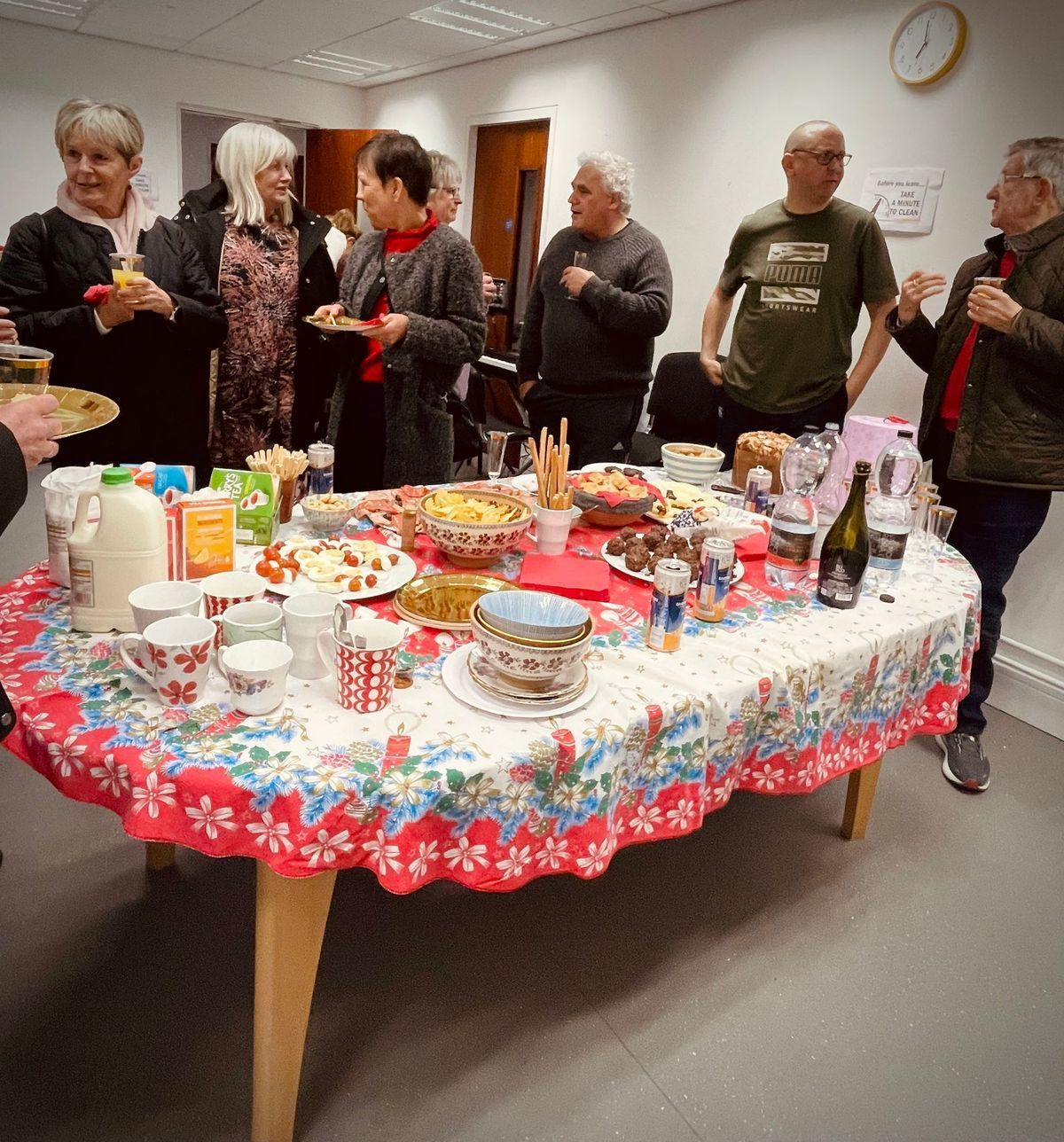 People gathered around a festive table with tea cups, snacks, and a colorful cloth in a bright room.