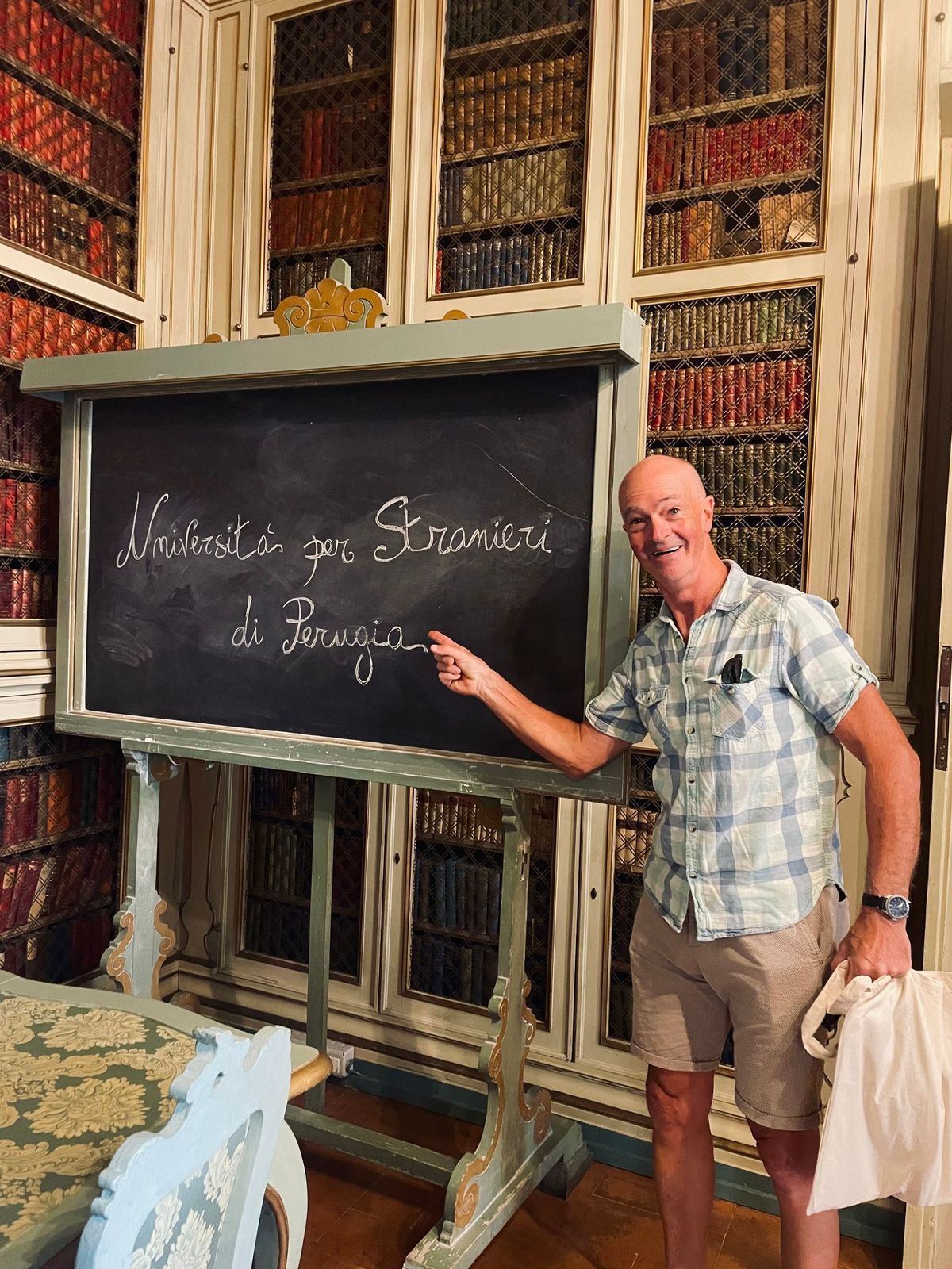 Man pointing at a chalkboard in a library with tall bookshelves and an old wooden display case