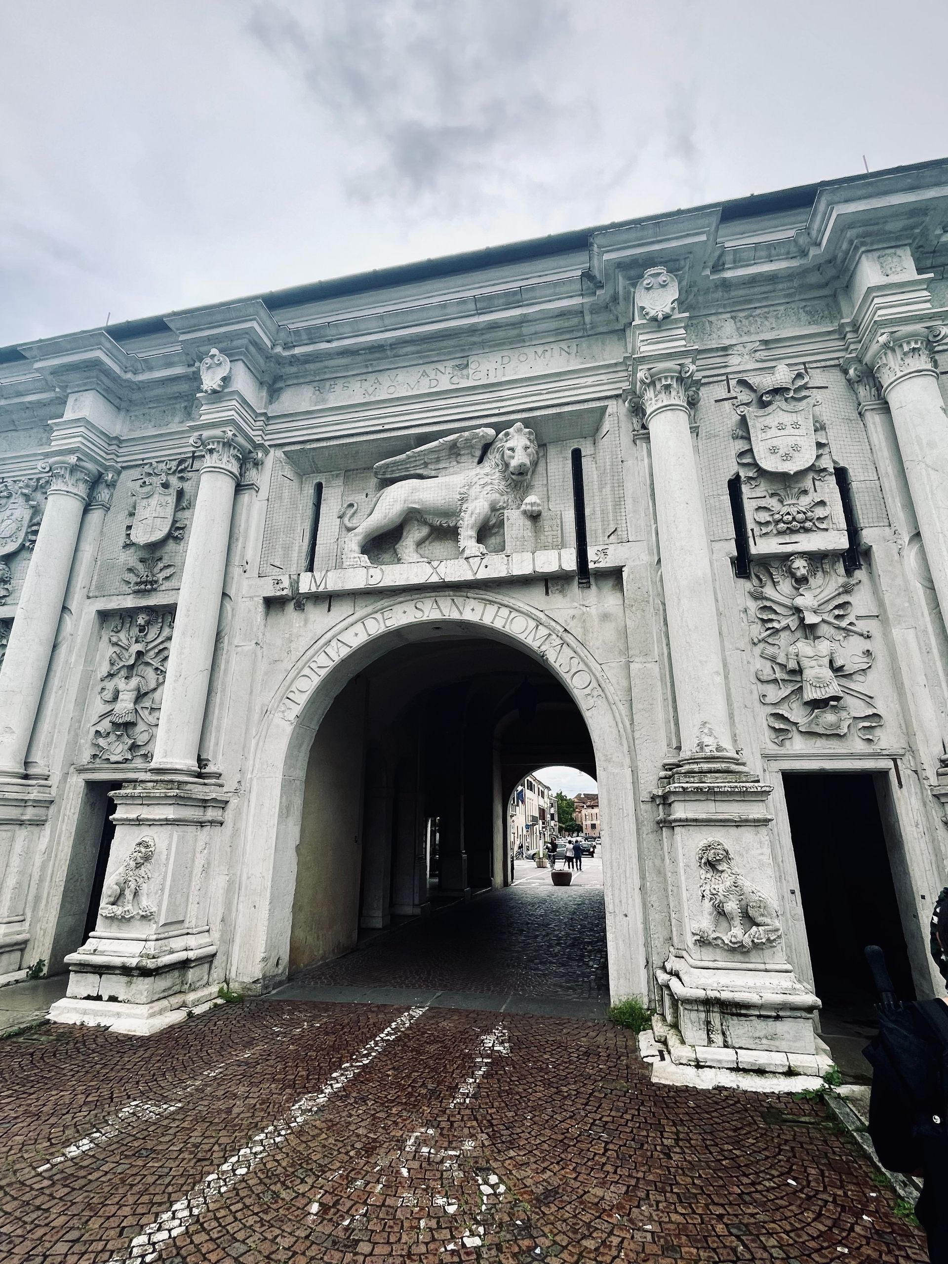 Ornate white stone archway with a lion relief and a cobblestone path leading through it