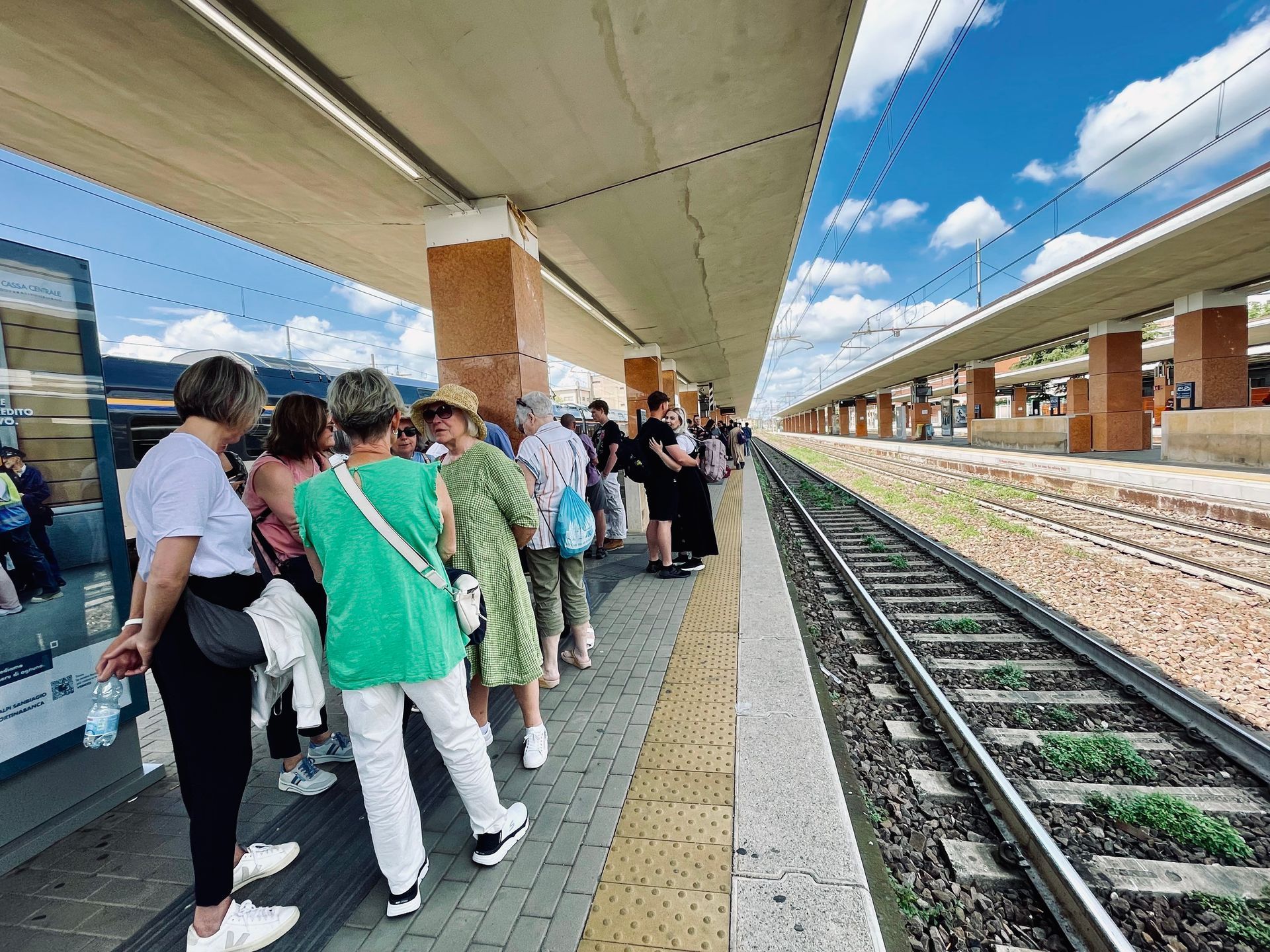 Crowded train platform with people waiting beside tracks under a covered station roof