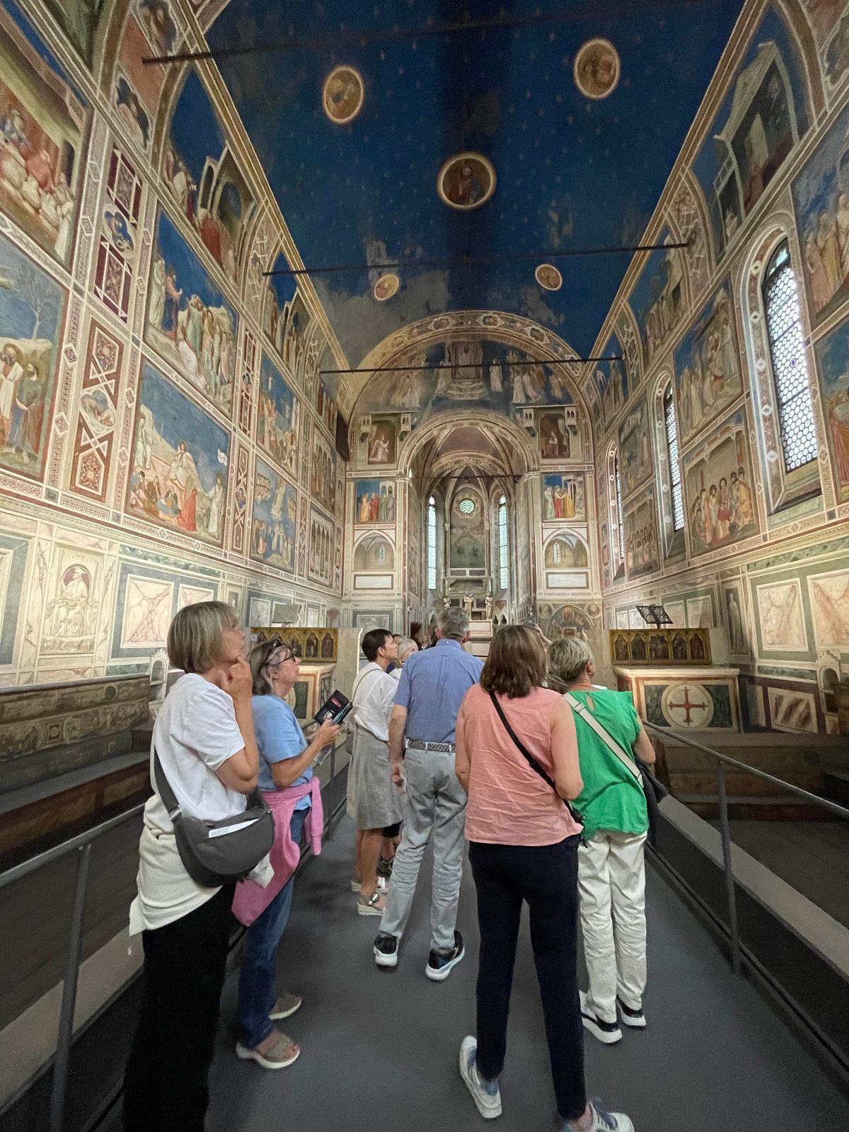 Visitors walking through an ornate frescoed hall with a vaulted blue ceiling and marble floor