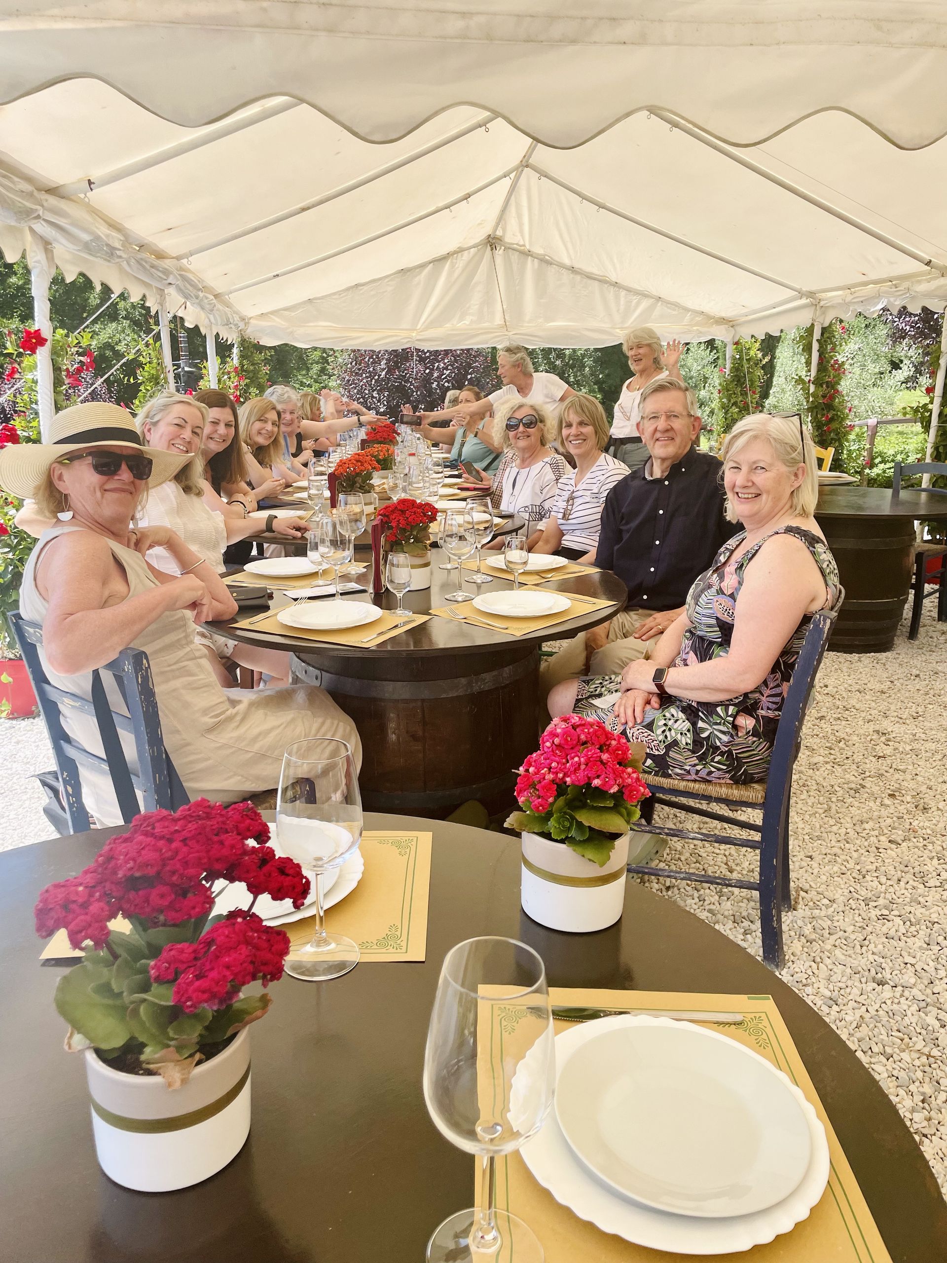 Guests seated at a decorated outdoor table under a white tent, enjoying a formal meal