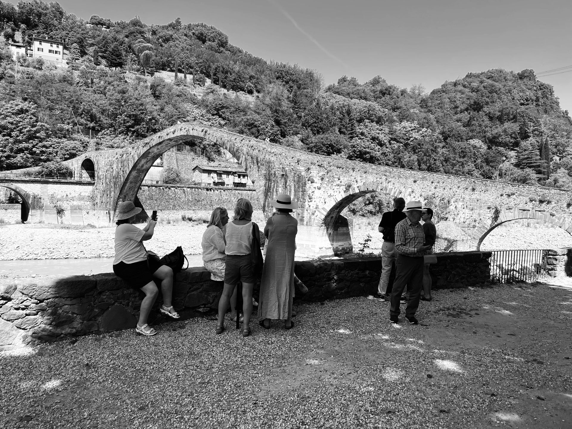 People standing and sitting by stone arches in a scenic outdoor ruin with hills in the background