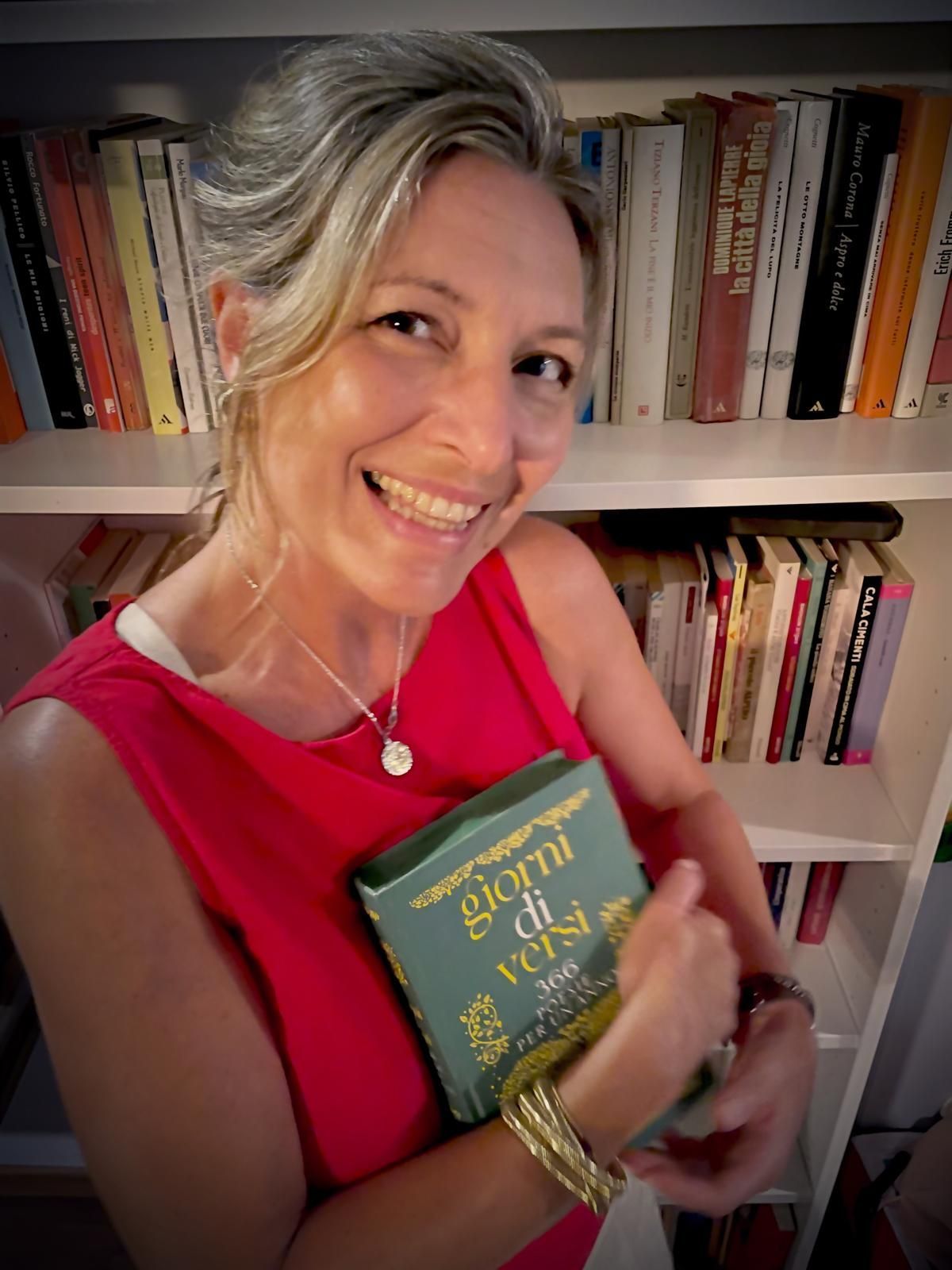 Woman in a red dress smiling and holding a green book in front of a bookshelf