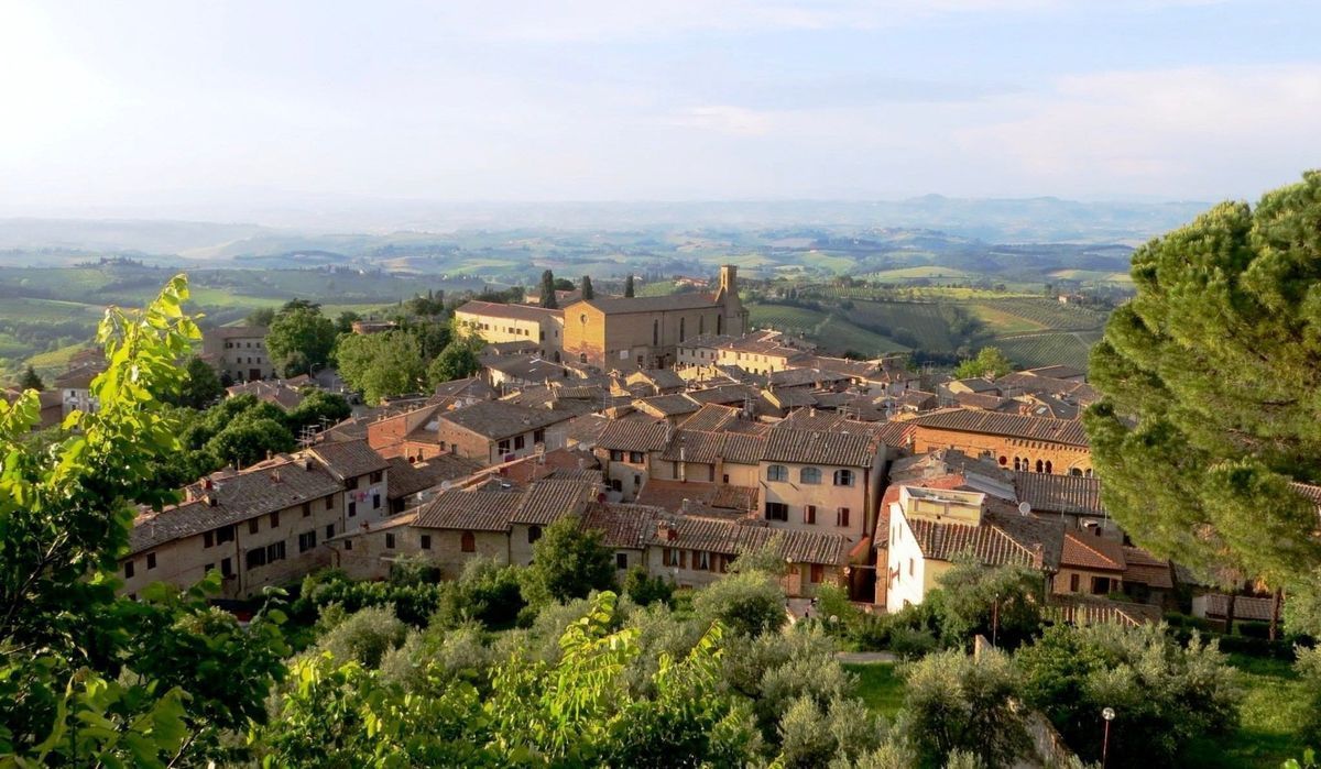 Hilltop village with terracotta rooftops overlooking a green valley and distant mountains under a clear sky