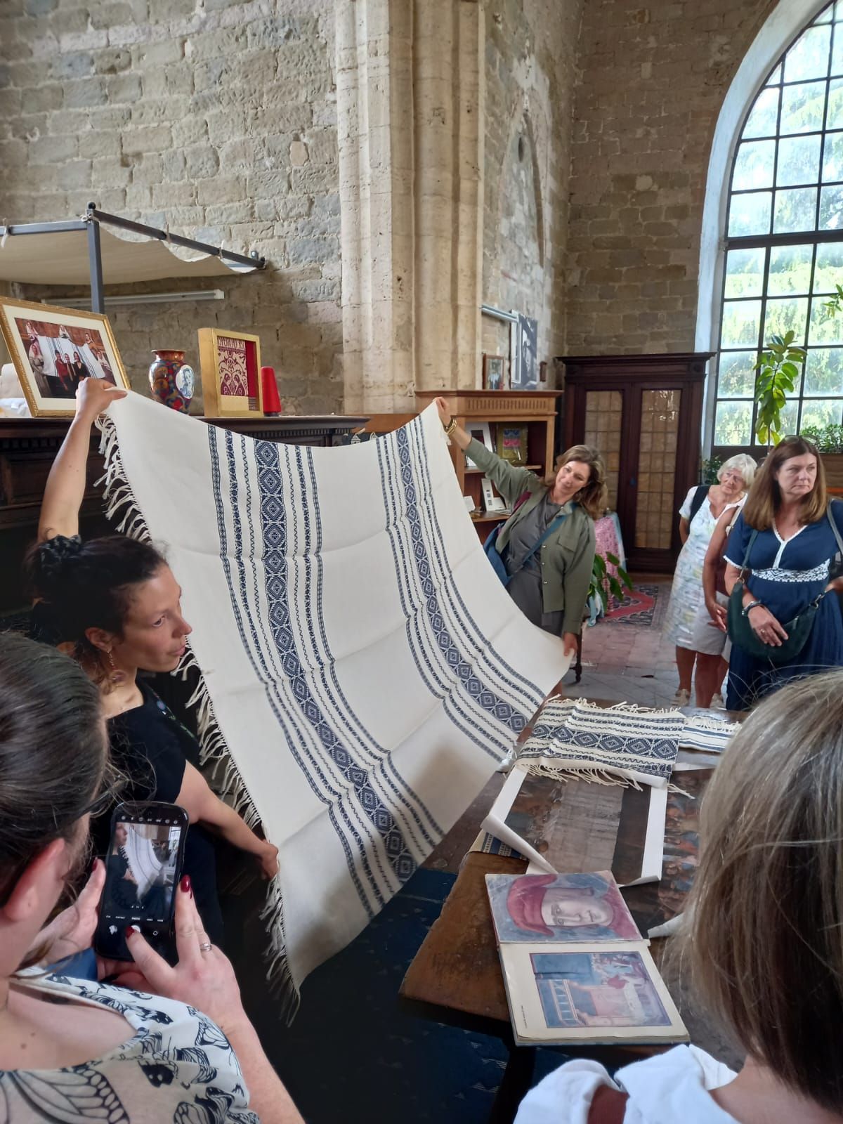 People holding up a striped woven textile in a stone gallery with large arched windows