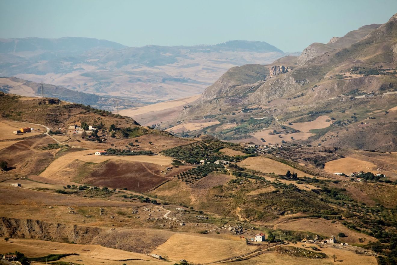 Paesaggio montano arido con colline terrazzate marroni e una valle avvolta dalla foschia in lontananza