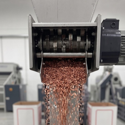 Gránulos de cobre cayendo desde una máquina procesadora de metales sobre una cinta transportadora.