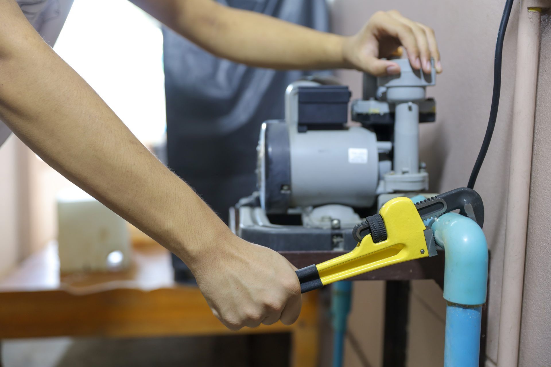 Person cleaning a gray motor with a yellow brush on a workbench near blue piping