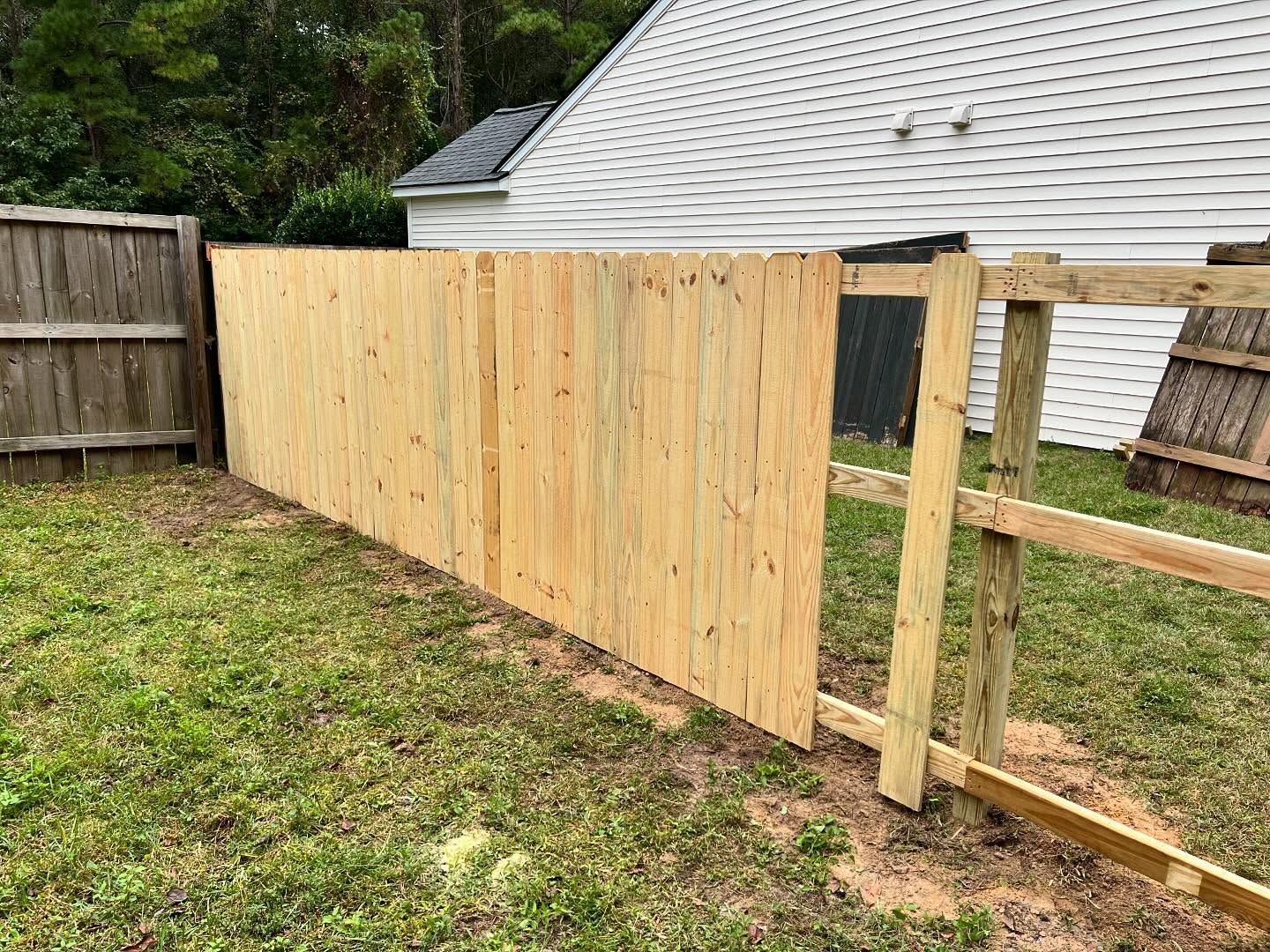 Wooden fence under construction in a backyard beside a house and grass lawn
