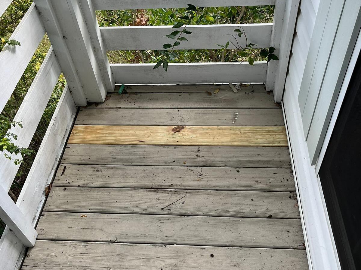 Weathered wooden porch floor with white railings and one lighter replacement board.
