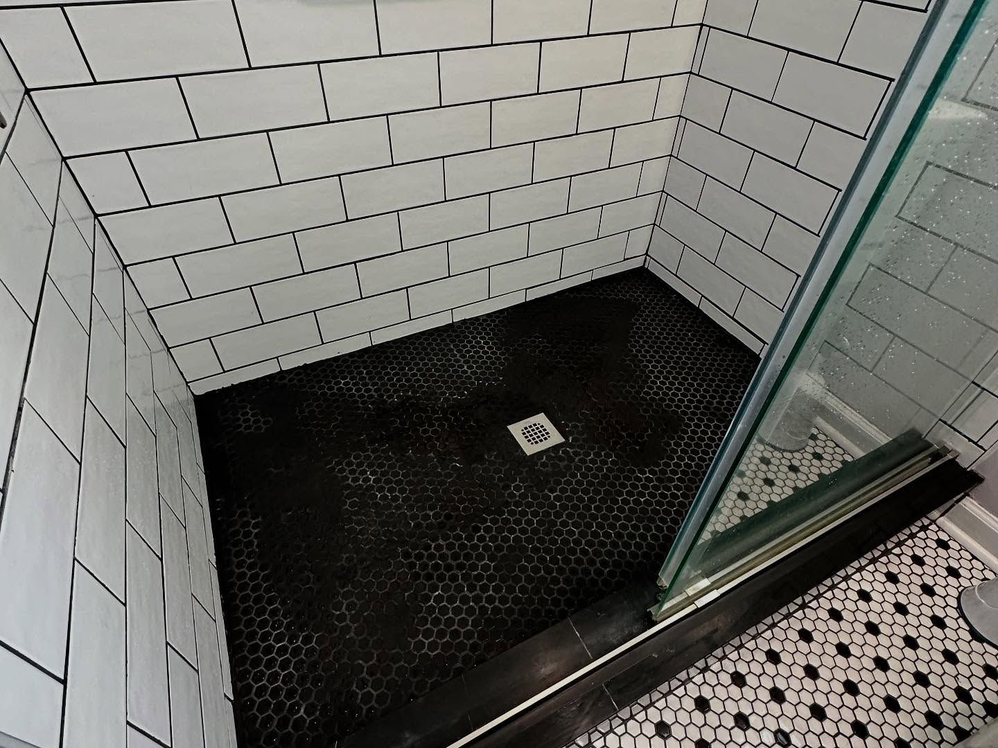 Tiled shower stall with black textured floor and glass door.