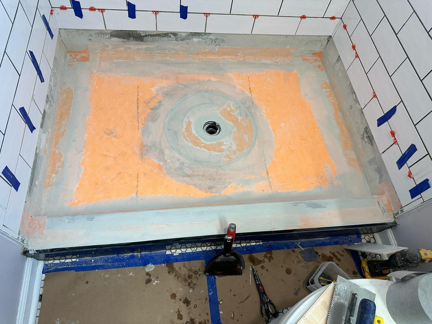 Bathroom sink basin being waterproofed with orange and gray coating, centered drain visible.