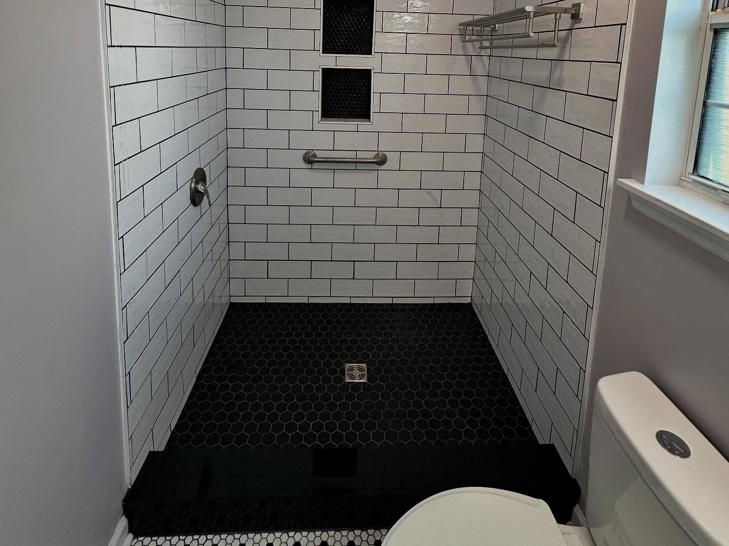 Small tiled bathroom shower stall with white subway walls, black floor, and a window at the back.