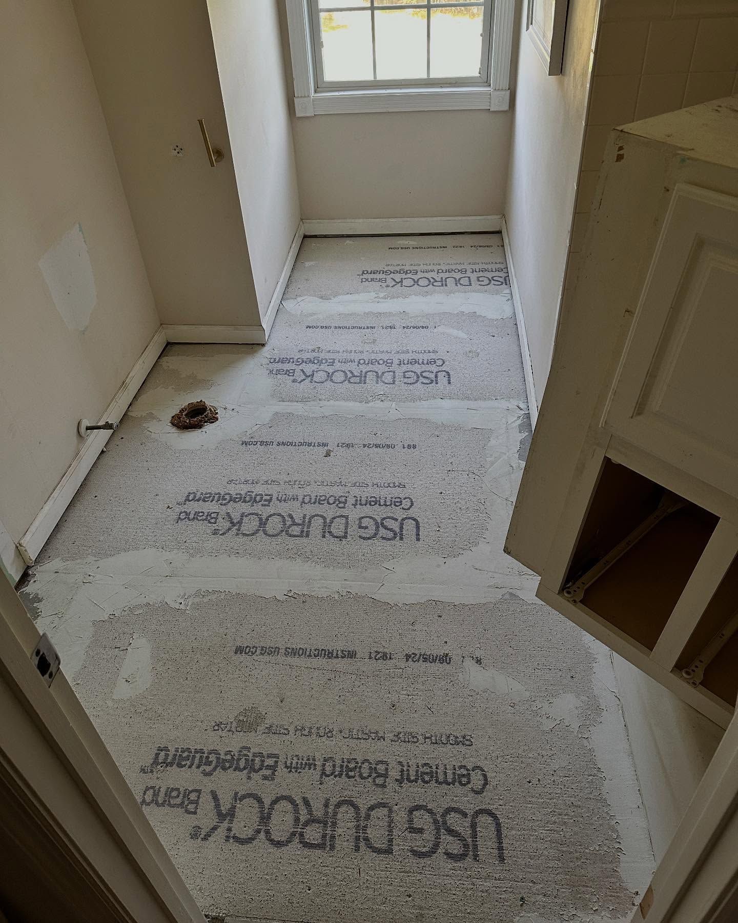 Bathroom floor covered with protective paper during renovation, near a window and vanity cabinet.