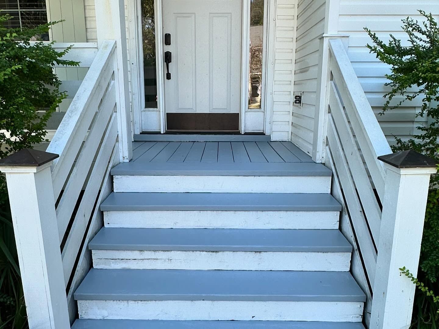 Front steps painted light blue leading to a white front door with railings and shrubs on both sides