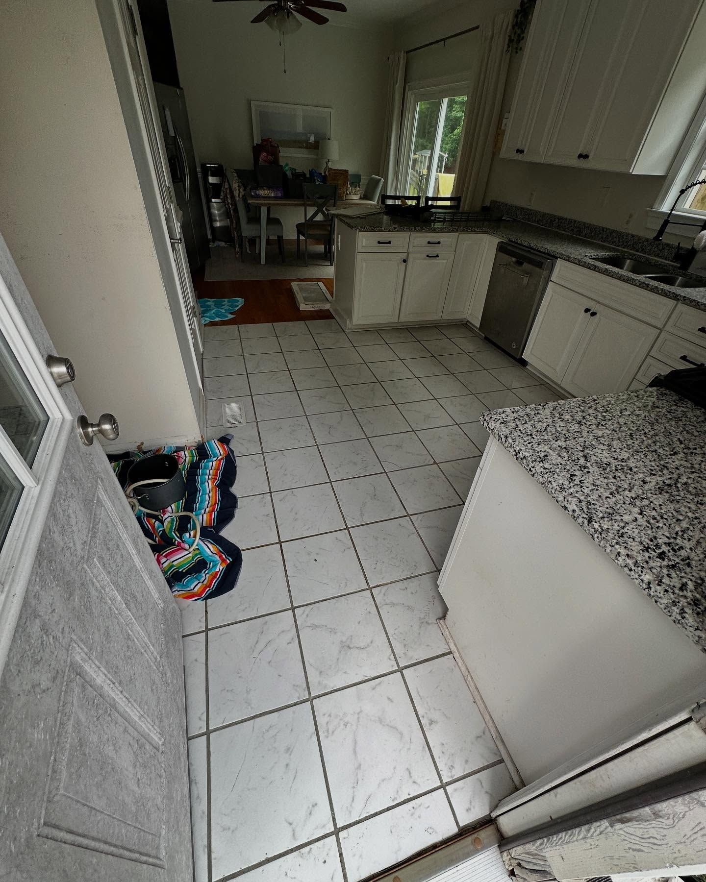 Narrow kitchen with white tiled floor, granite counters, cabinets, and a colorful bag on the floor.