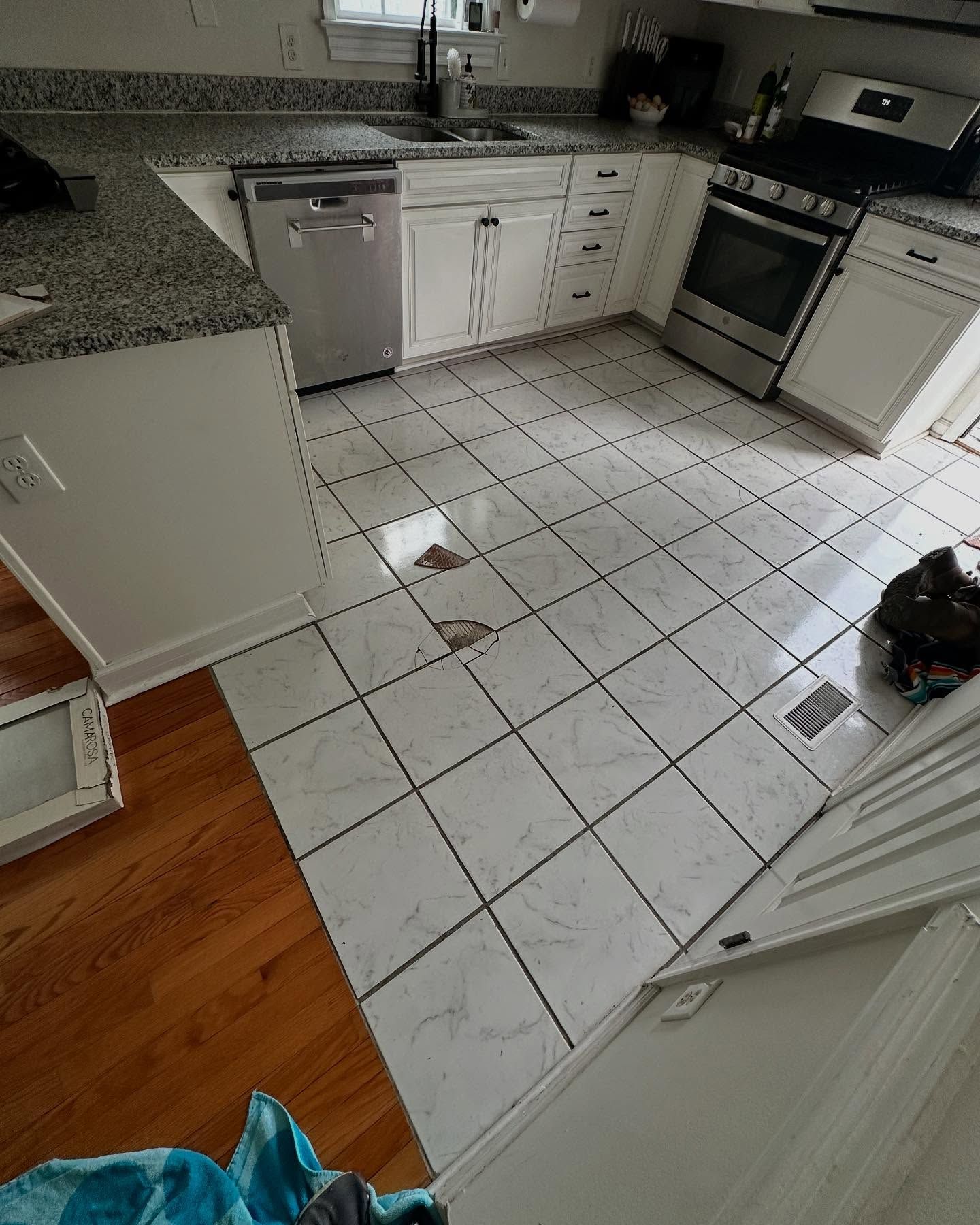 Kitchen with white tile floor, dishwasher, stove, cabinets, and a brown spill near the center.