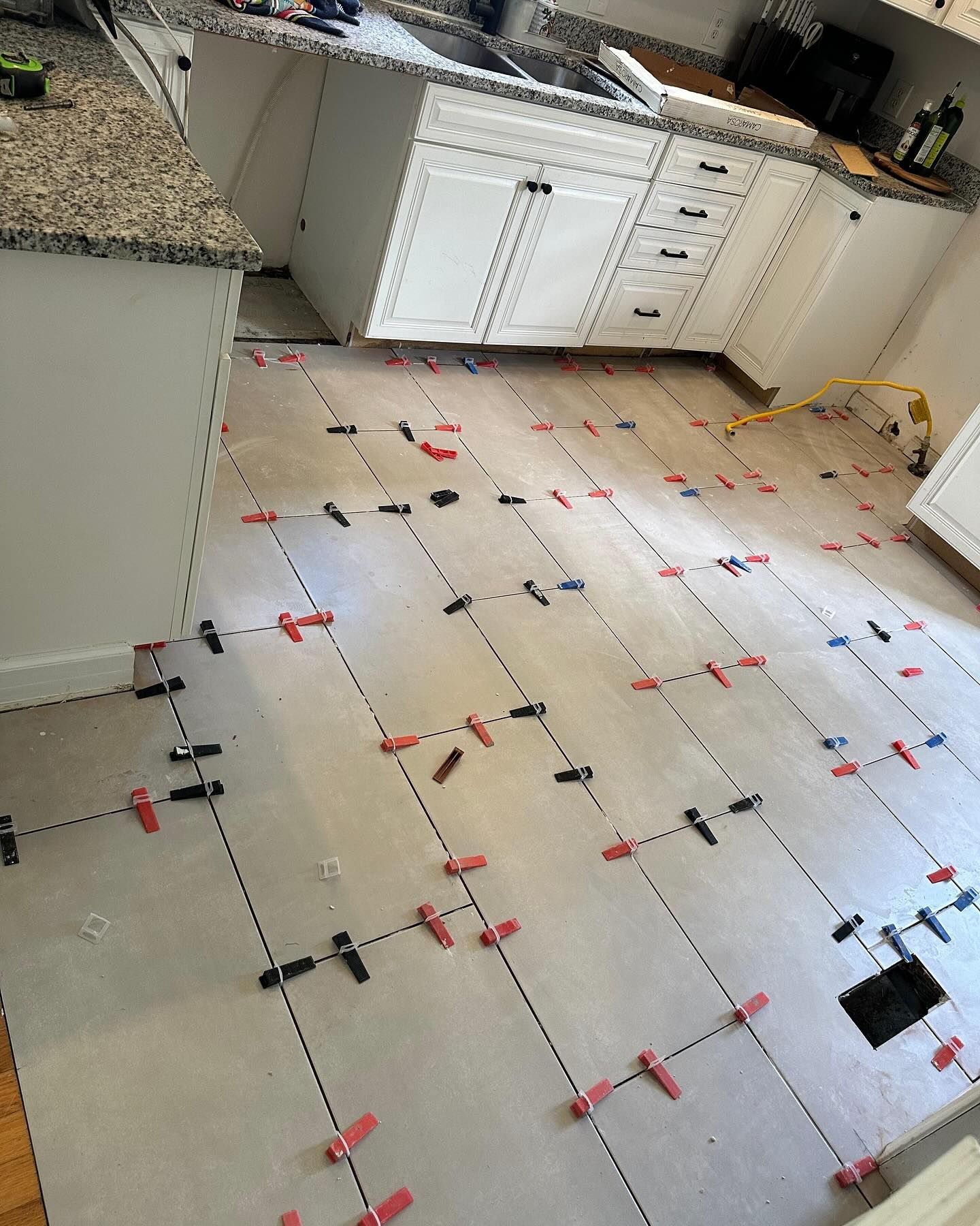 Kitchen floor covered with large white tiles marked by red and black spacers during installation