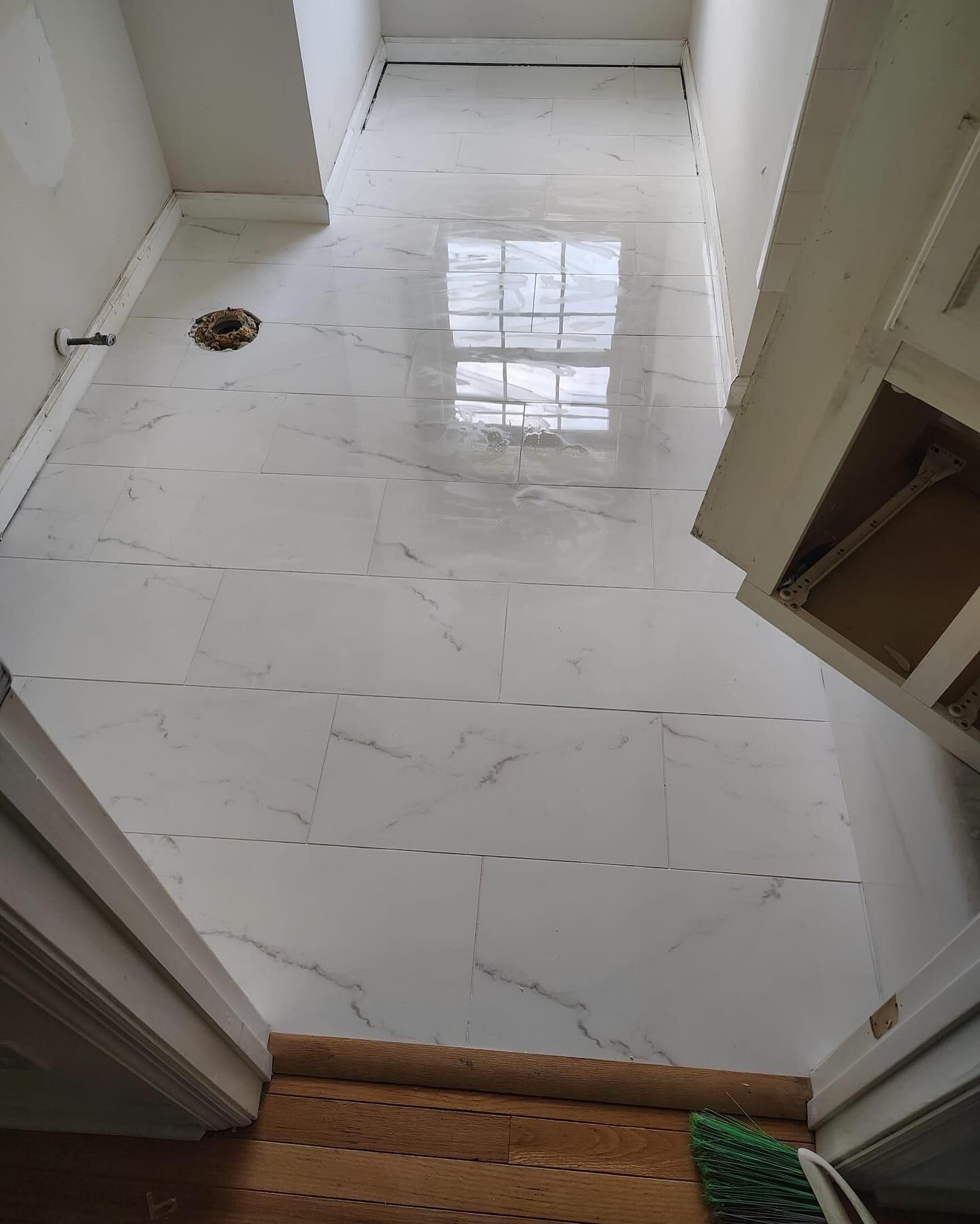 White-tiled hallway with a small floor drain and a wooden step at the bottom